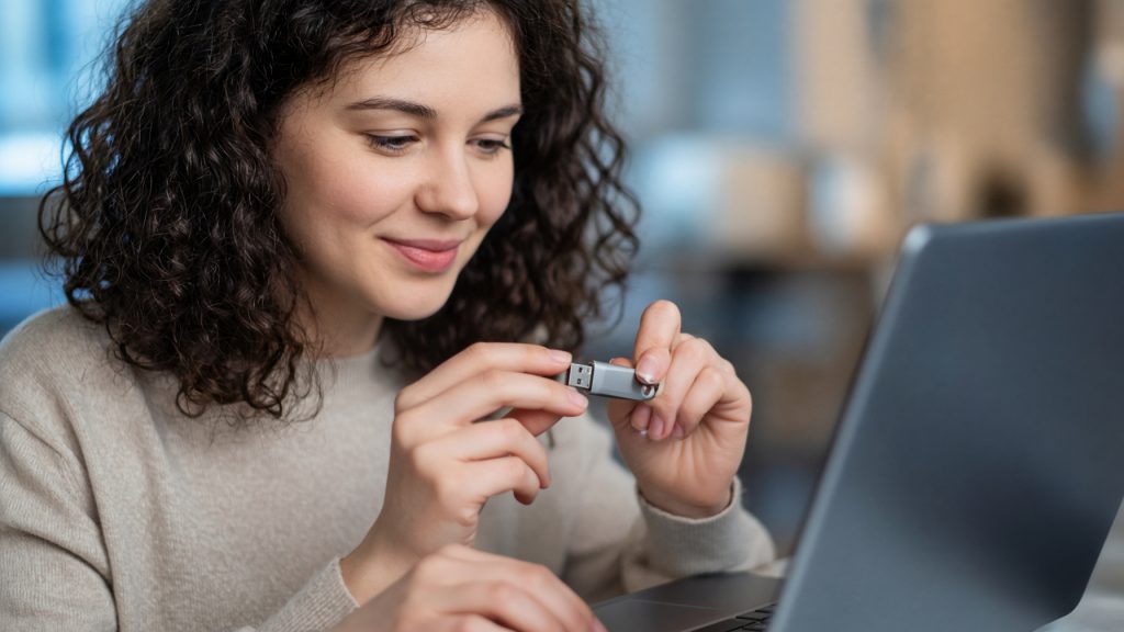 A woman inserting a metal USB flash drive into the side port of a laptop